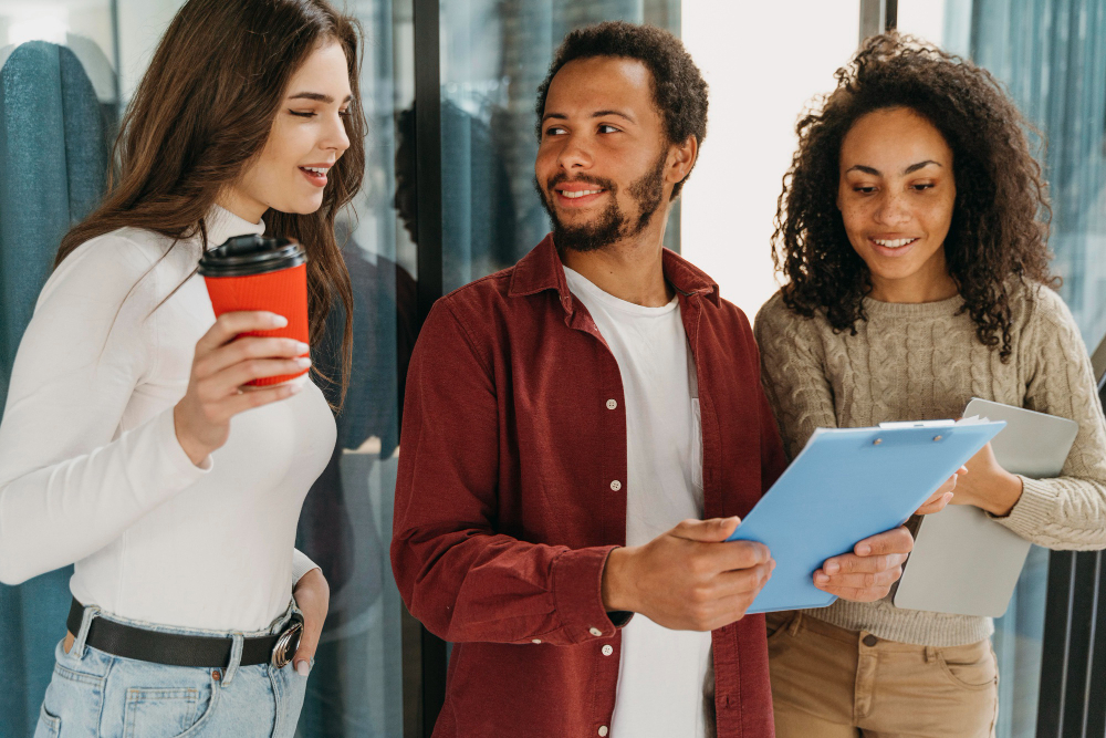 Trio de jovens discutindo ideias com documentos, representando o recrutamento de jovens talentos.