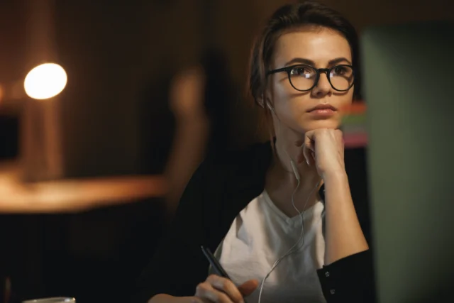 Mulher com óculos e fones de ouvido, concentrada em frente a um computador, pesquisando sobre a consultoria de executive search.